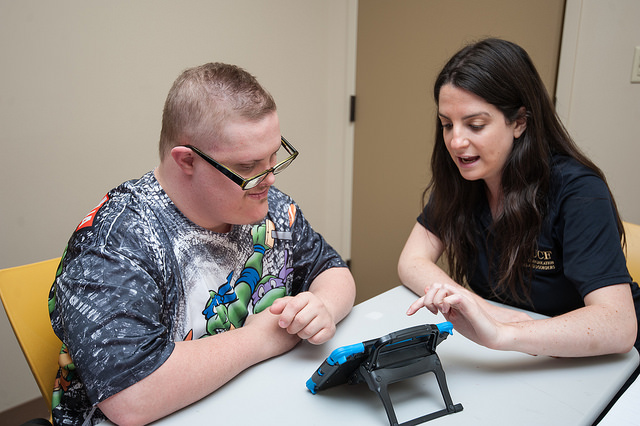 UCF student using a tablet for Augmentative and Alternative Communication with a young male