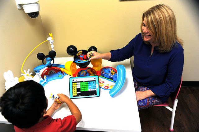 faculty member assisting a young child with language skills while using a digital tablet