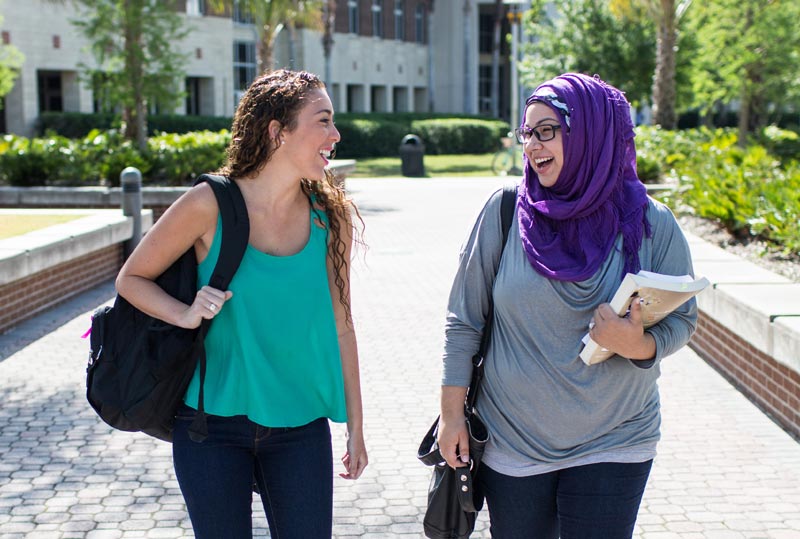 two students talking and laughing while walking on campus