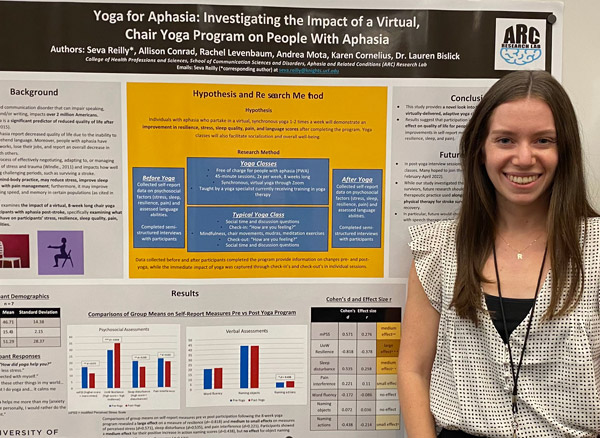a female student standing next to their research poster on the impact of yoga on people with aphasia