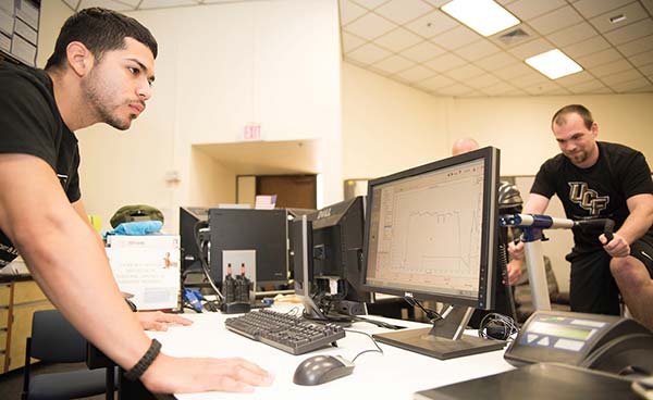 student researchers reviewing data while another student is using a stationary bike