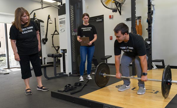 Student researchers taking notes while one student lifts weights