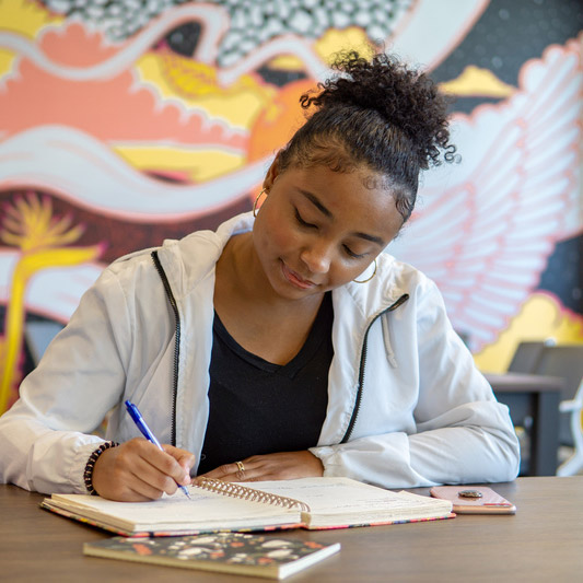 female student sitting in a desk and writing in a notebook