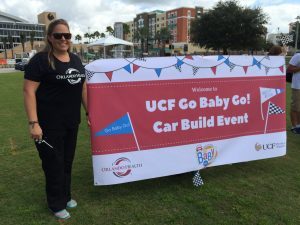 UCF alumna Lindley Westervelt in front of a banner that says, "UCF Go Baby Go! Car Build Event."