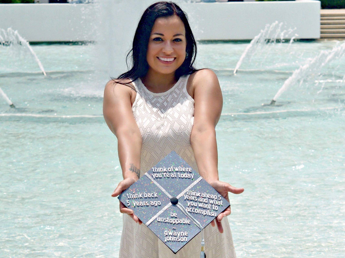 Heather Robison in front of the Reflection Pond holding her graduation cap in front of her.