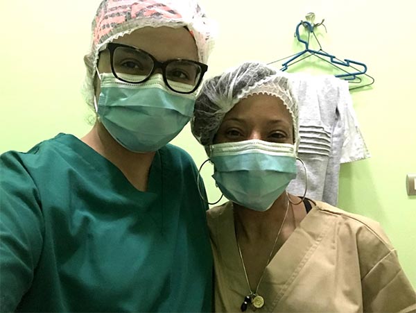Two women wearing masks, scrubs and medical hair caps.