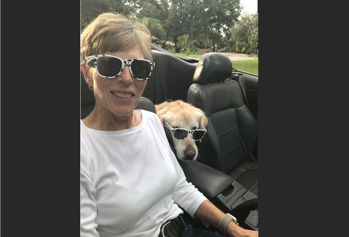 Gail Kauwell riding in a car with her dog wearing sunglasses