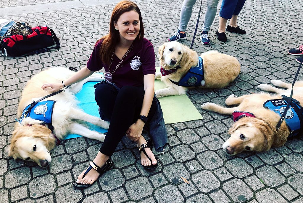 woman seated with three golden retriever therapy dogs