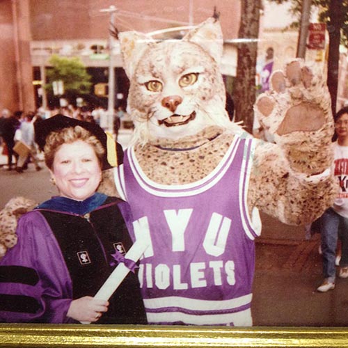 Ana in cap and gown while posing with NYU mascot.