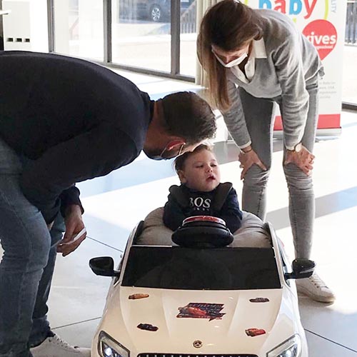 Two adults checking in on a little boy in an adapted ride-on toy car.