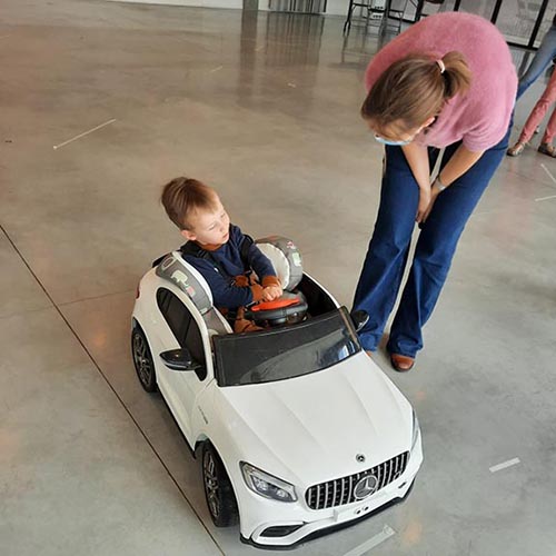 A woman checking in on a little boy in a ride-on toy car.