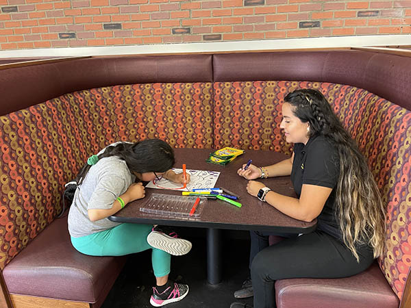 CSD clinician talking to child with coloring book across a booth