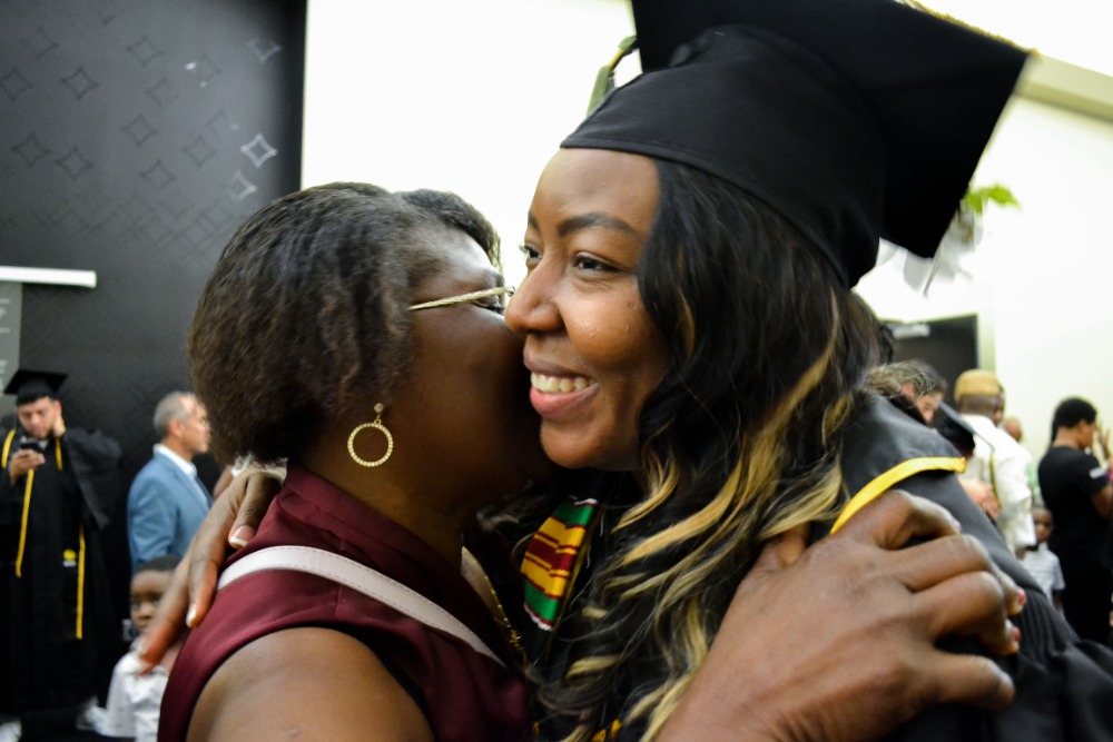 BSW student in graduation regalia hugging woman.