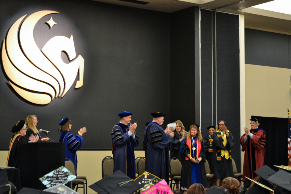 UCF Faculty in graduation regalia on stage during a graduation celebration, standing ovation for Sophia Dziegielewski who is emotional.