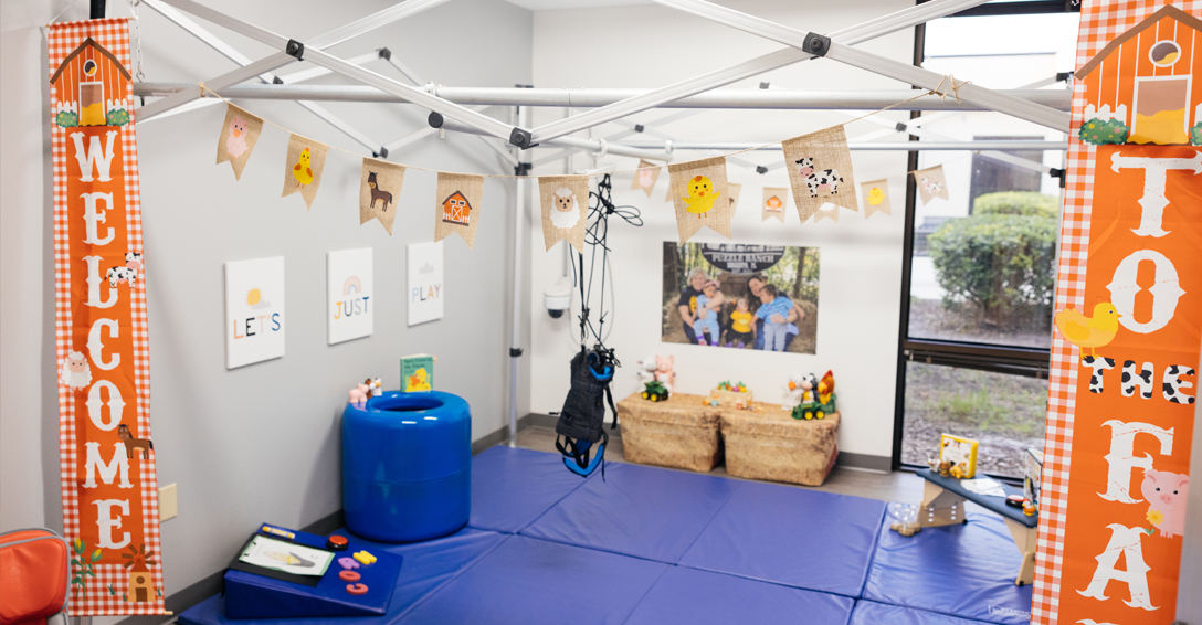 Mobile harness system in playroom with toys and mats on ground.