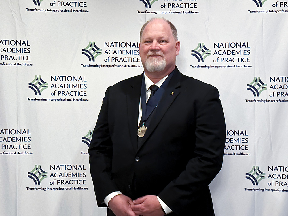 Founding Dean Ingersoll standing with a medal around his neck and smiling at camera