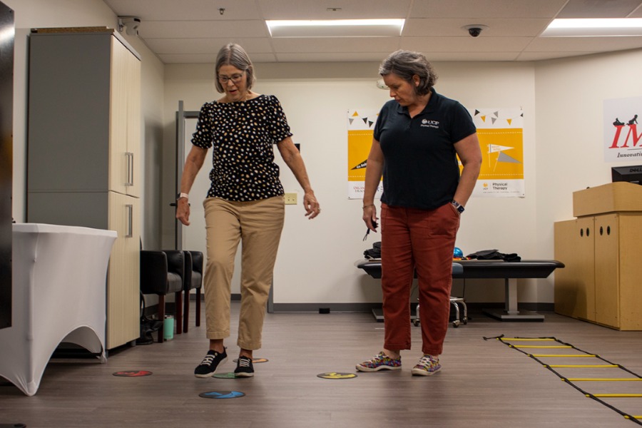 woman walking in physical therapy and woman standing beside monitoring