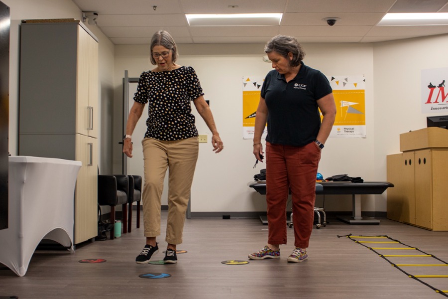 Woman walking in physical therapy and woman standing beside monitoring.