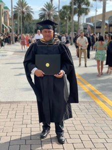 Allfonso Tejeira standing in cap and gown with diploma