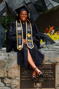 Angela Jarman in cap and gown sitting on statue base