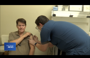 Parker Baro bending over giving vaccine in the arm of a man while he holds his shirt sleeve up