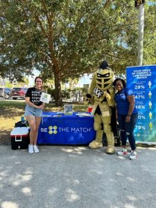 Sydney Martinez, Knightro and other student standing with Be The Match table