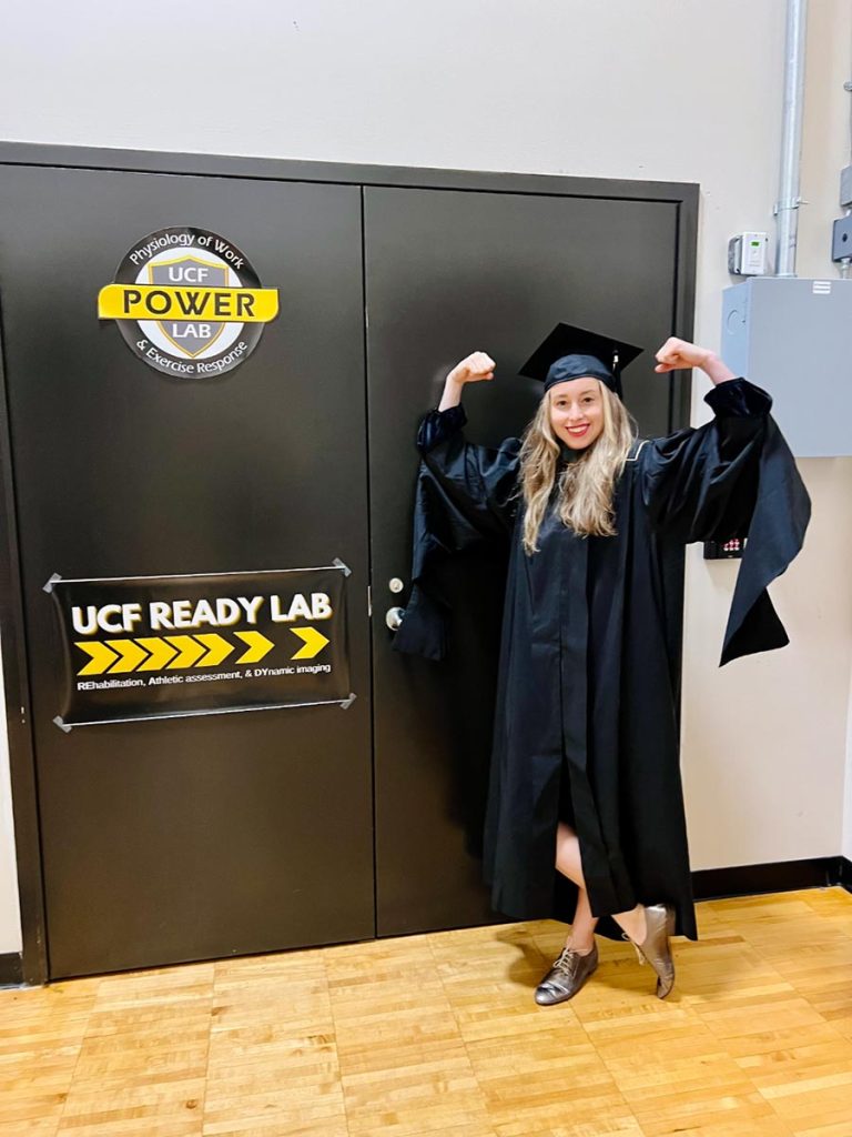 Bonnie Kerlin flexing her biceps in front of UCF's READY Lab.