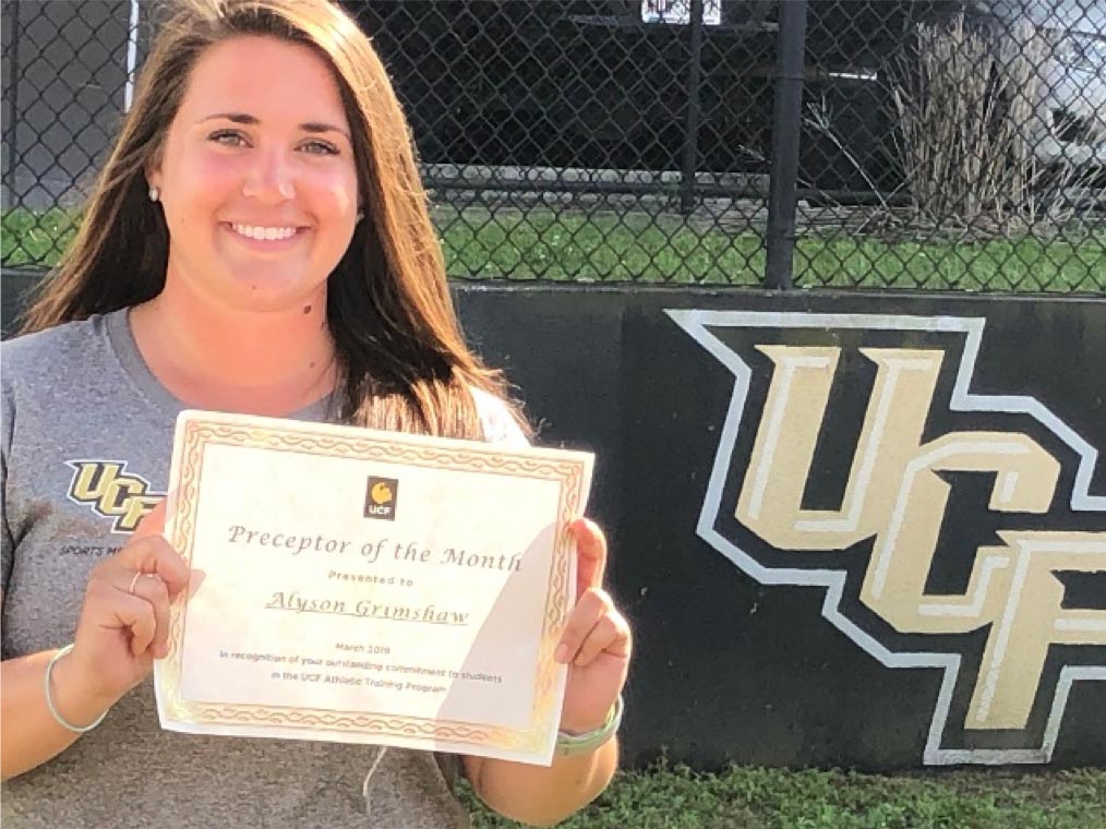 Alyson Grimshaw holding a certificate in front of UCF Banner.