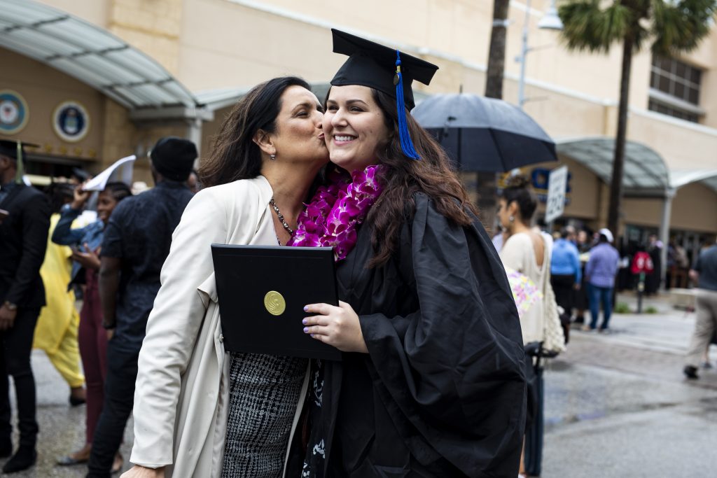 Mom kissing daughter, who is wearing cap and gown, on cheek