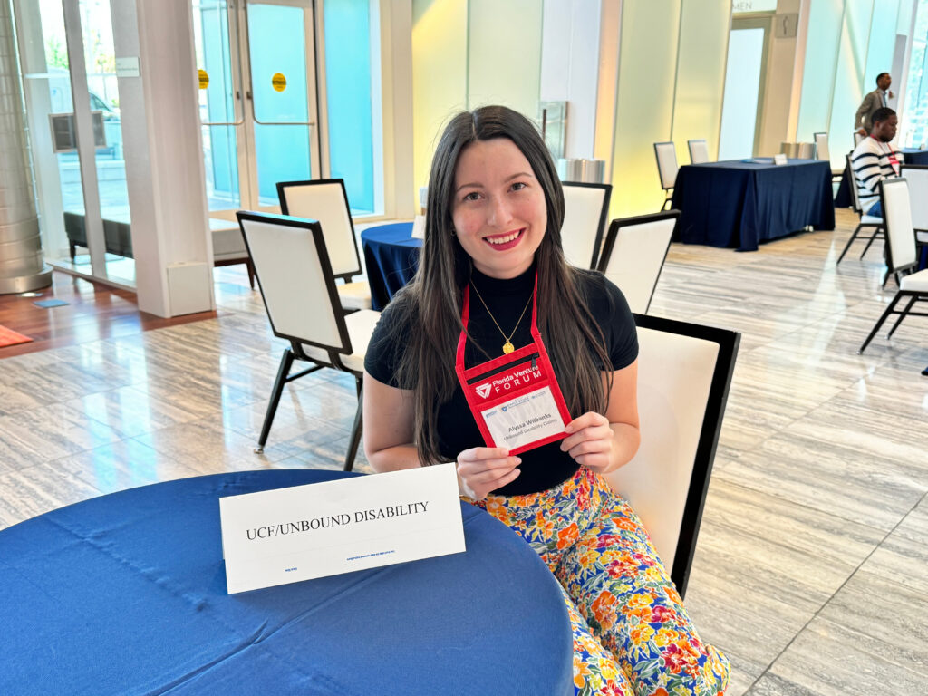 Senior health sciences major Alyssa Wilbanks sits at a table, representing Unbound Disability Claims at the Florida Venture Forum.