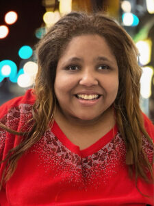 Ashlei McGhee smiles while wearing a red sweater with lights in the background. 