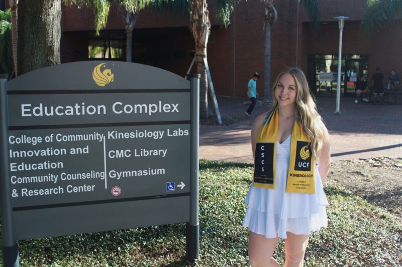 Hannalee smiles and poses to the right of an Education Complex sign.