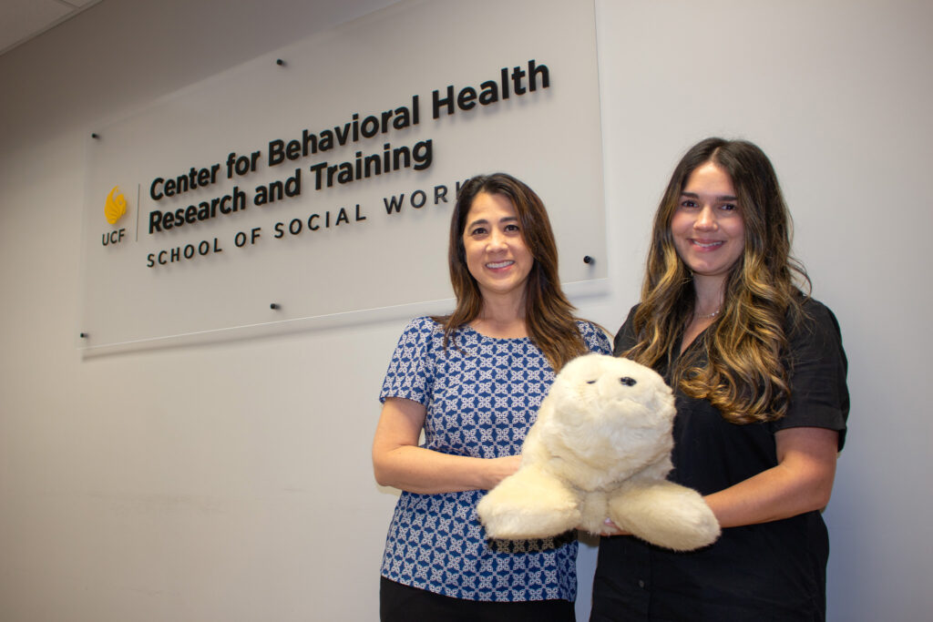 Professor Kim Gryglewicz (left) and Associate Professor Susanny Beltran (right) hold Sully the Seal, the College of Health Professions and Sciences’ first PARO therapeutic robot.