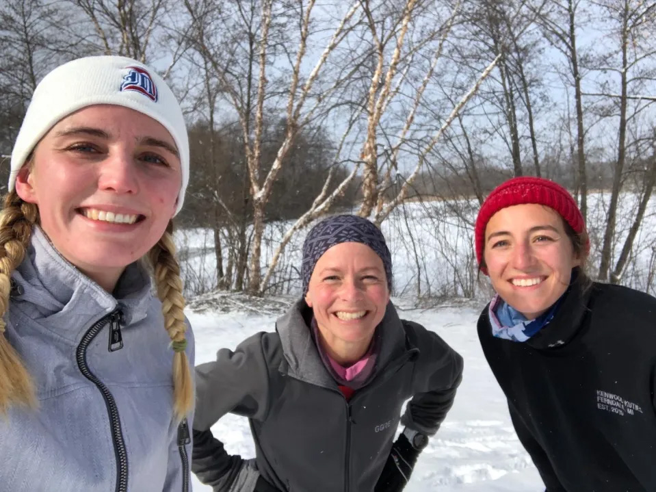 Three women in hats smile in the snow.