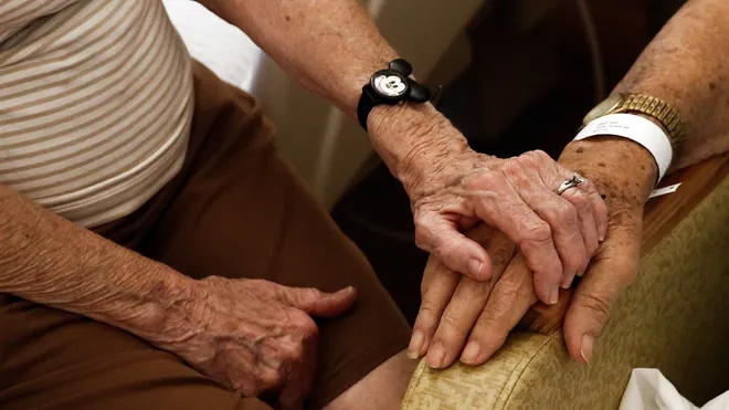 two elderly people hold hands