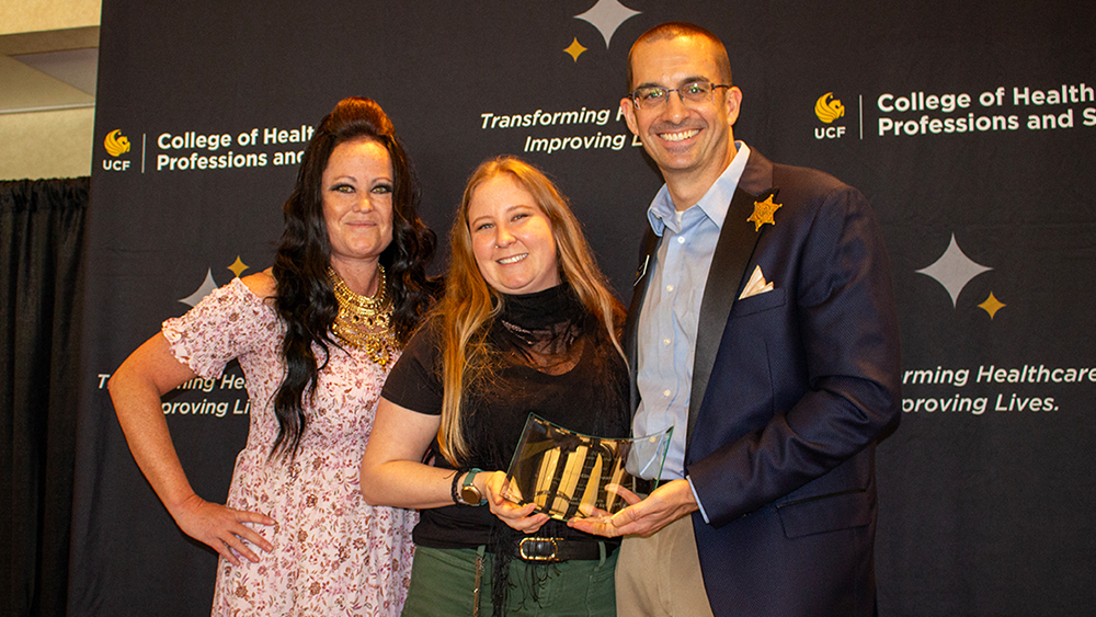 Annie Parker, Christina Grosso, and Matthew Theriot smiling in front of a CHPS backdrop while Christina holds her award