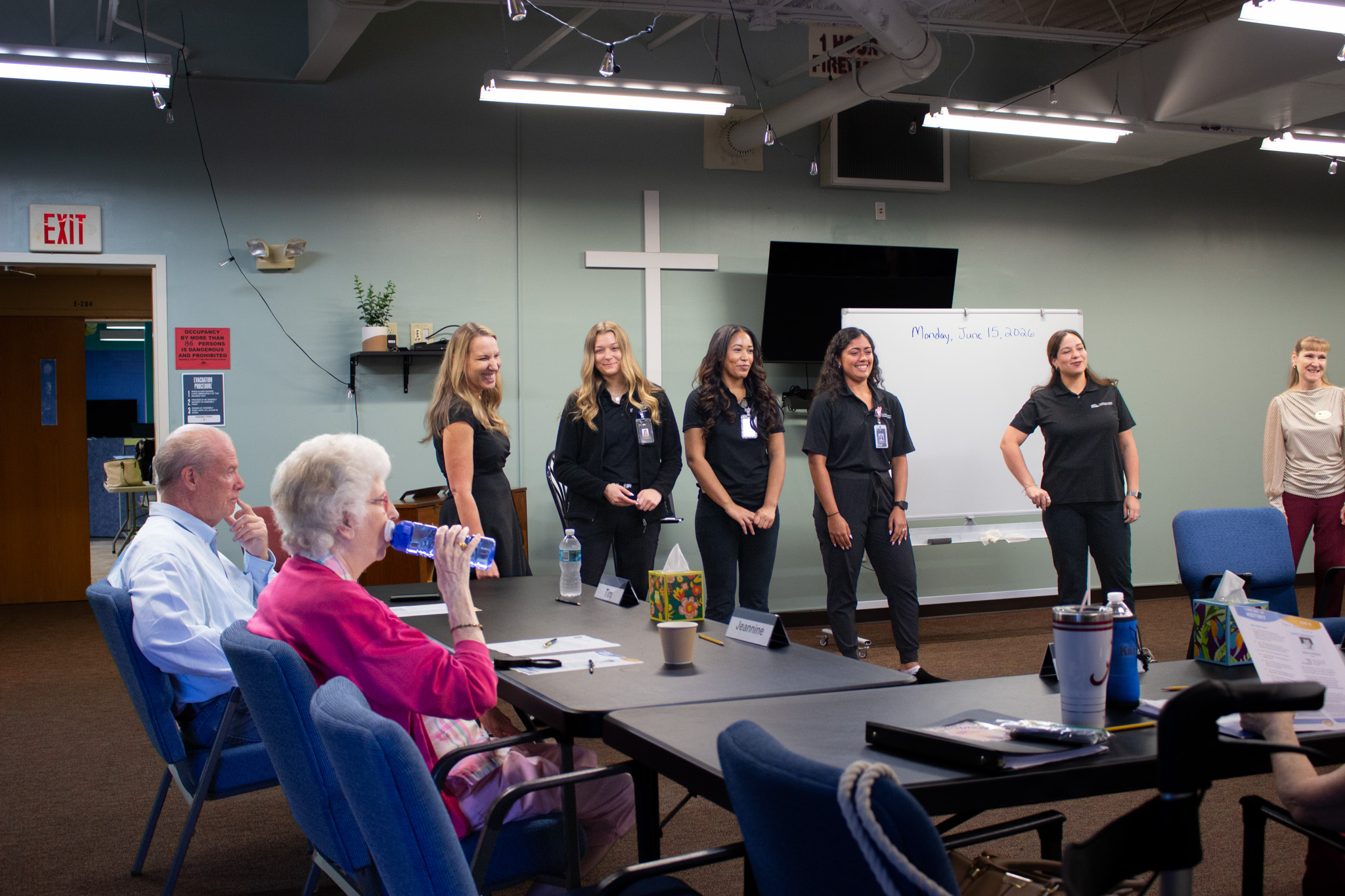 A group of women in black scrubs stand in front of a man in a blue shirt and a woman in a pink shirt