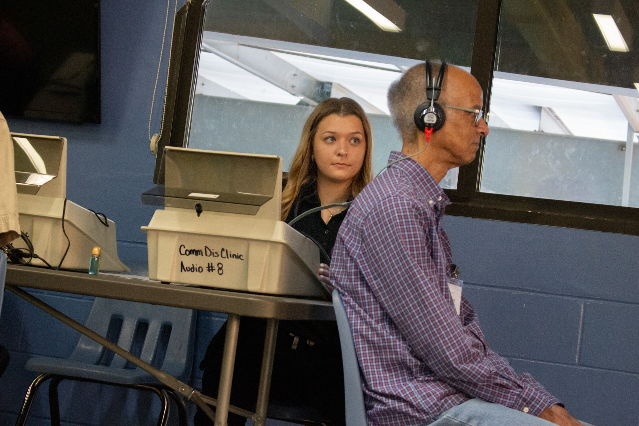 A man in a purple sits while wearing headphones.