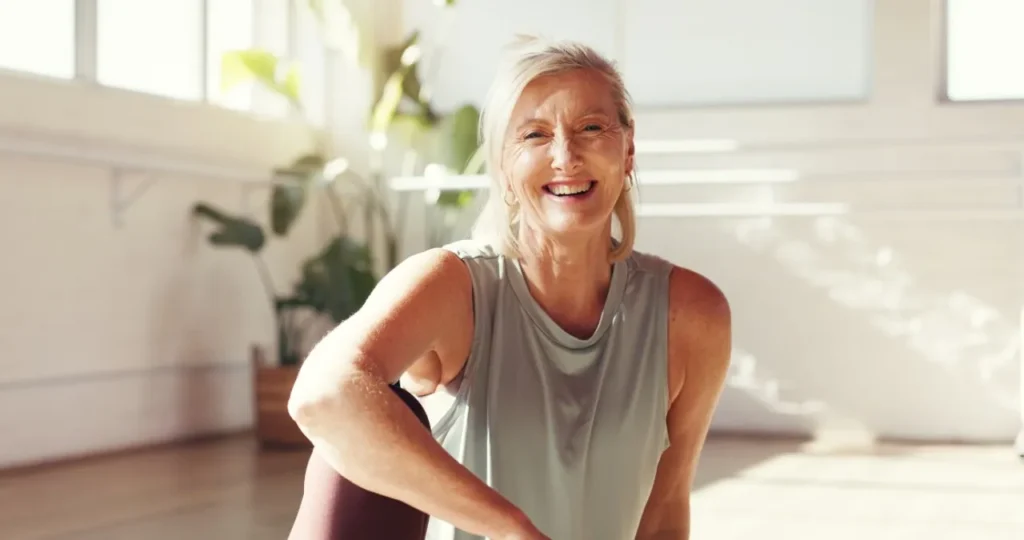 a woman in a gray tank top smiles while sitting on the floor