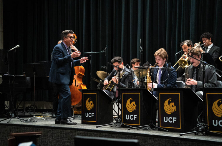 A man conducting a UCF band on stage as the band plays their instruments